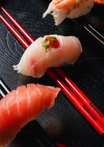 three pieces of salmon sushi laid across red Benihana branded chopsticks