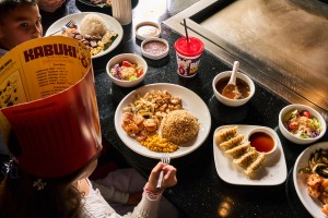 A child wearing a chef hat holding a fork, with a plate of hibachi food